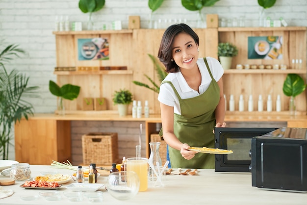 Jovem muito criativa secando fatias de laranja no micro-ondas enquanto prepara ingredientes de sabão orgânico