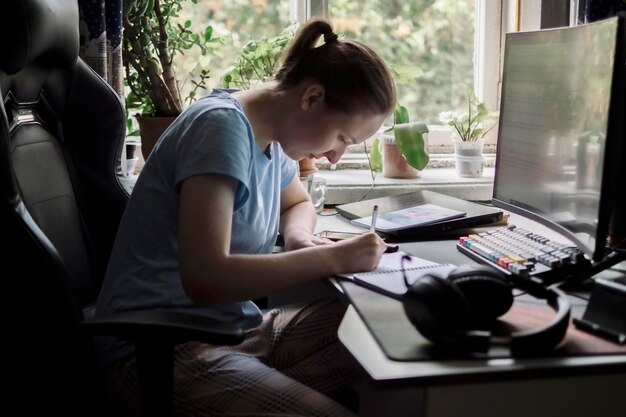 Jovem mulher a trabalhar no computador a escrever num caderno a fazer um curso on-line ou a treinar em casa