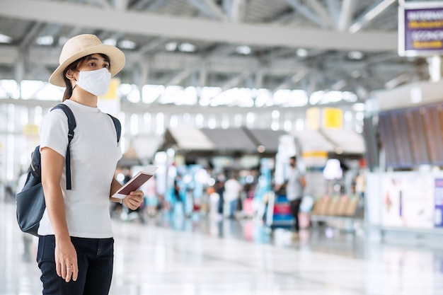 Jovem mulher adulta com máscara facial segurando passaporte no aeroporto