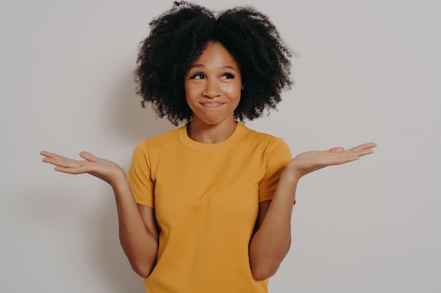 Jovem mulher africana em pé com expressão confusa sem noção e engraçada com braços e mãos levantadas