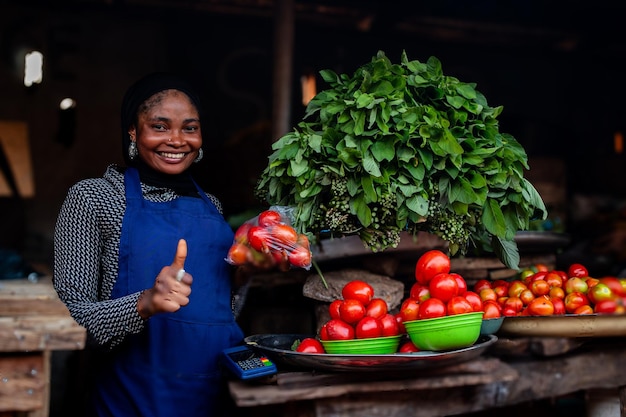 Jovem mulher africana no mercado a vender tomates a levantar o polegar