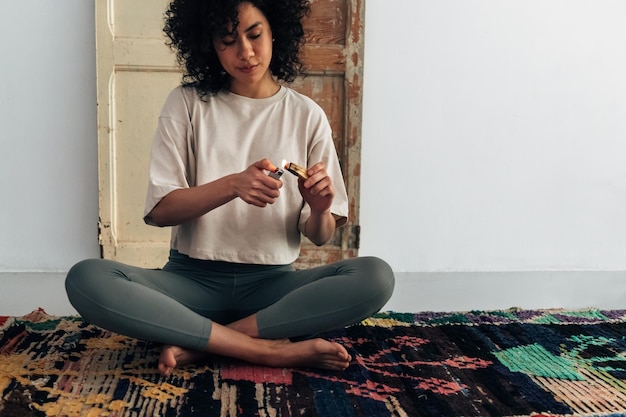 Foto jovem mulher afro-americana acendendo palo santo com isqueiro para limpar a sala e meditar copiar espaço conceito de espiritualidade e saúde mental