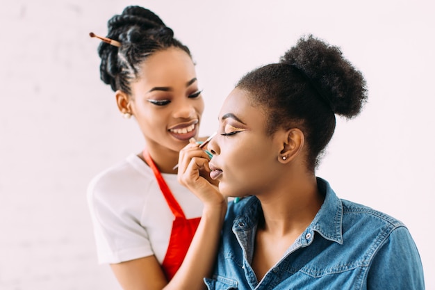 Jovem mulher afro-americana bonita aplicar maquiagem profissional pelo maquiador Africano. Sessão de estúdio