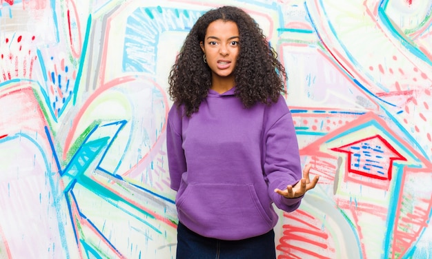 Jovem mulher afro-americana bonita olhando com raiva contra a parede do graffiti