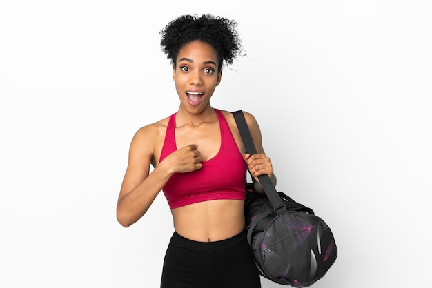 Jovem mulher afro-americana com bolsa esportiva isolada em um fundo azul e expressão facial surpresa.