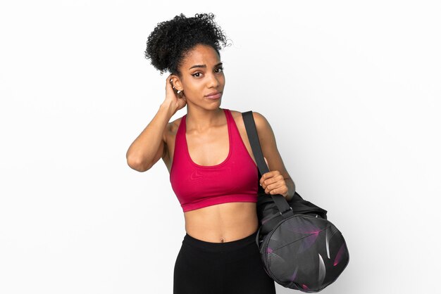 Jovem mulher afro-americana com bolsa esportiva isolada em um fundo azul, tendo dúvidas.