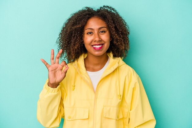 Jovem mulher afro-americana com cabelo encaracolado, isolado em um fundo azul alegre e confiante, mostrando o gesto de ok.