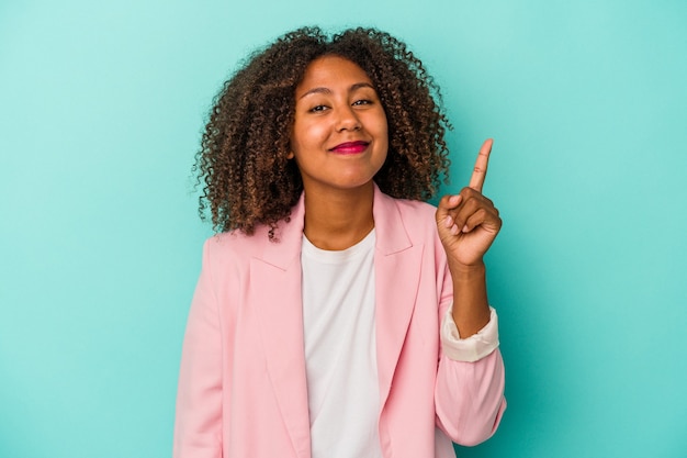 Jovem mulher afro-americana com cabelo encaracolado isolado em um fundo azul, mostrando o número um com o dedo.