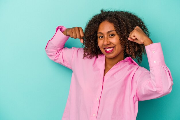 Jovem mulher afro-americana com cabelo encaracolado, isolado no fundo azul torcendo despreocupada e animada. Conceito de vitória.