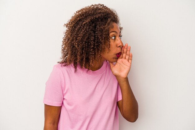 Jovem mulher afro-americana com cabelo encaracolado, isolado no fundo branco está contando uma notícia secreta sobre a travagem e olhando para o lado