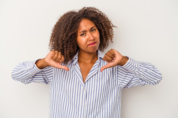 Jovem mulher afro-americana com cabelo encaracolado, isolado no fundo branco, mostrando o polegar para baixo, conceito de decepção.