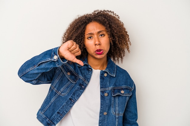 Jovem mulher afro-americana com cabelo encaracolado, isolado no fundo branco, mostrando o polegar para baixo e expressando antipatia.