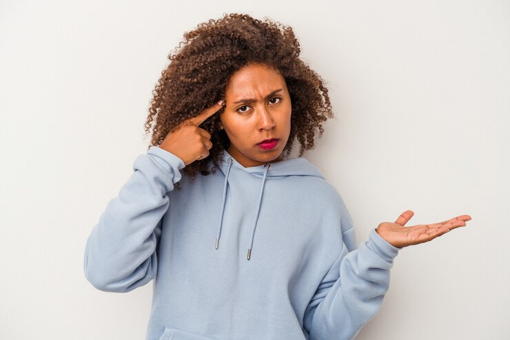 Foto jovem mulher afro-americana com cabelo encaracolado, isolado no fundo branco, mostrando um gesto de decepção com o dedo indicador.