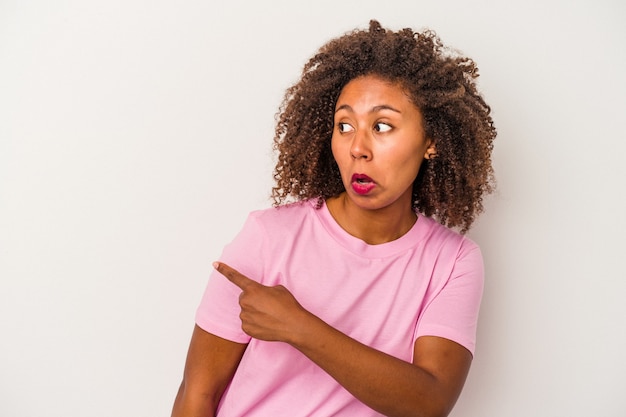 Jovem mulher afro-americana com cabelo encaracolado, isolado no fundo branco, sorrindo e apontando de lado, mostrando algo no espaço em branco.