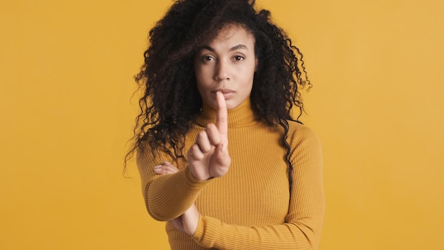 Jovem mulher afro-americana com cabelo escuro e fofo parecendo confiante contando pelos dedos na câmera sobre fundo amarelo Contando o gesto