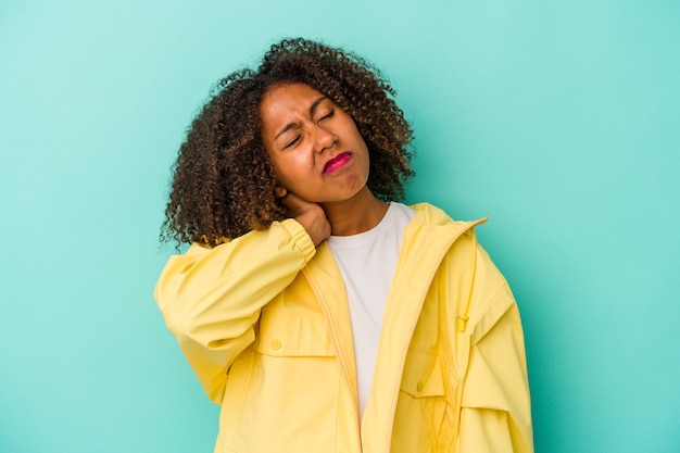 Jovem mulher afro-americana com cabelos cacheados, isolado em um fundo azul, tendo uma dor de garganta devido ao estresse, massageando e tocando-o com a mão.