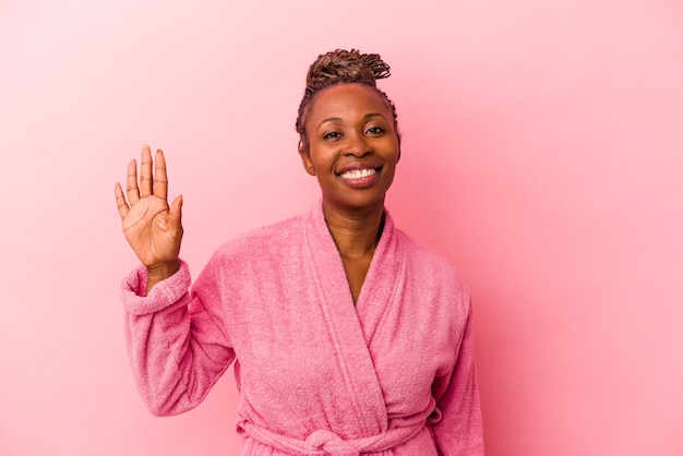 Jovem mulher afro-americana com roupão rosa isolado no fundo rosa, sorrindo alegre mostrando o número cinco com os dedos.