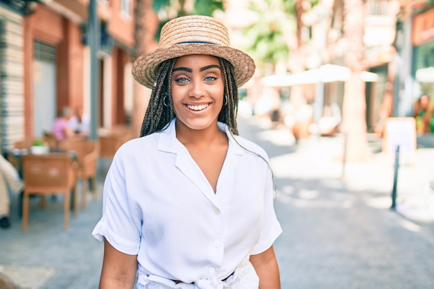 Jovem mulher afro-americana com tranças sorrindo feliz ao ar livre em um dia ensolarado de verão