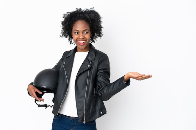 Jovem mulher afro-americana com um capacete de moto na parede branca segurando copyspace imaginário na palma da mão