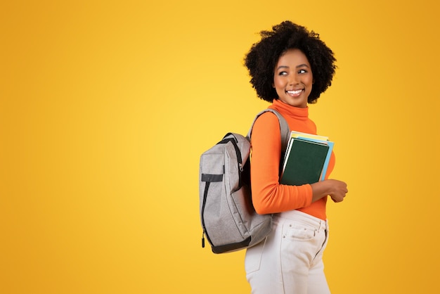 Jovem mulher afro-americana confiante com um sorriso encantador carregando uma mochila cinzenta e colorida