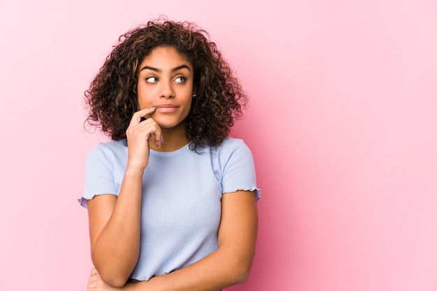 Foto jovem mulher afro-americana contra uma parede rosa jovem mulher afro-americana contra uma parede rosa relaxada pensando em algo olhando para um espaço de cópia.