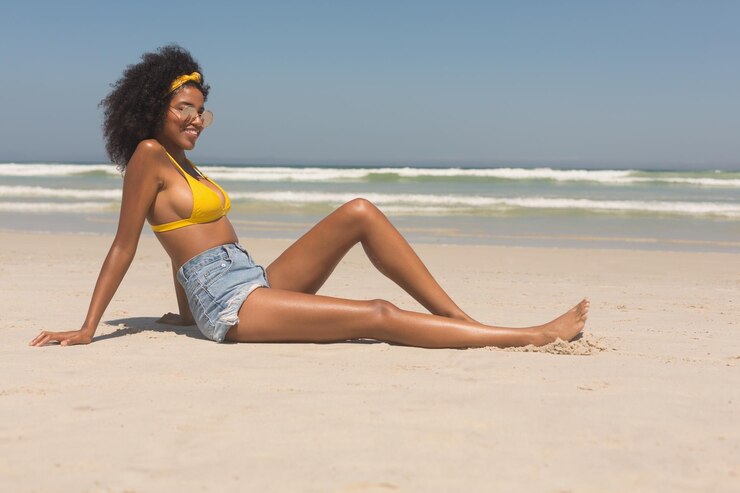 Foto jovem mulher afro-americana de biquíni amarelo e óculos de sol relaxando na praia