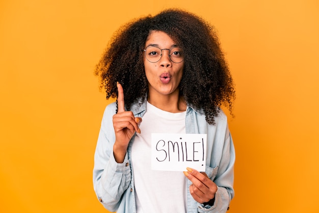 Jovem mulher afro-americana encaracolada segurando um cartaz de mensagem de sorriso, tendo uma ótima ideia, o conceito de criatividade.