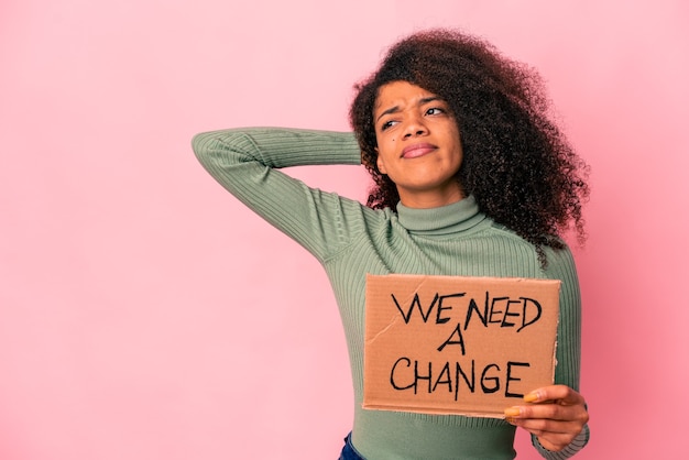 Jovem mulher afro-americana encaracolada segurando um precisamos de um papelão de mudança tocando a parte de trás da cabeça, pensando e fazendo uma escolha.
