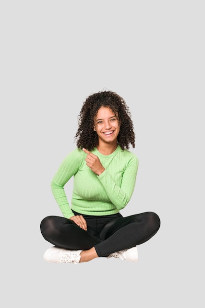 Jovem mulher afro-americana encaracolada sentada no chão isolada