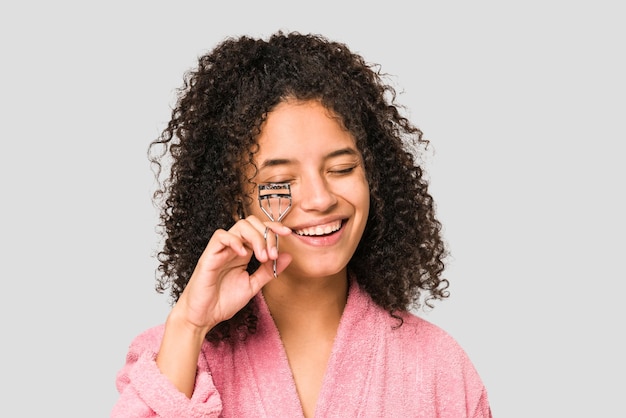 Jovem mulher afro-americana encaracolada usando um modelador de cílios isolado