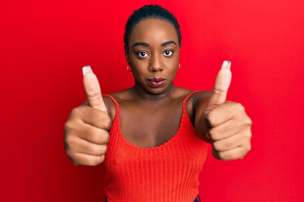 Jovem mulher afro-americana fazendo polegares para cima gesto positivo relaxado com expressão séria no rosto simples e natural olhando para a câmera