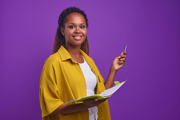 Jovem mulher afro-americana feliz segurando pasta aberta para documentos e caneta