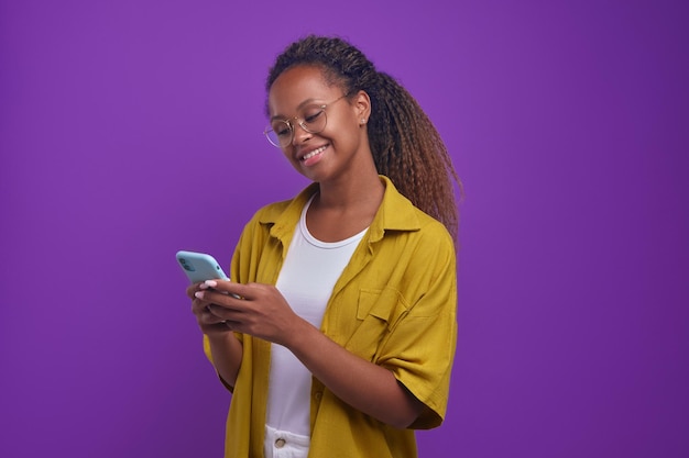 Jovem mulher afro-americana feliz usando telefone fica no estúdio roxo