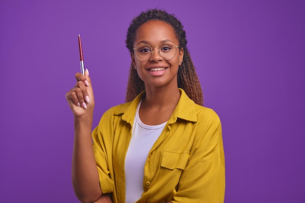 Jovem mulher afro-americana independente com grande sorriso levanta a mão com caneta