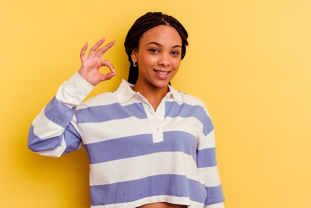 Jovem mulher afro-americana isolada em amarelo alegre e confiante, mostrando um gesto de ok.