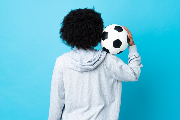 Jovem mulher afro-americana isolada em azul com bola de futebol