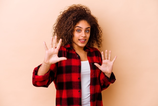 Jovem mulher afro-americana isolada em bege, rejeitando alguém mostrando um gesto de nojo.