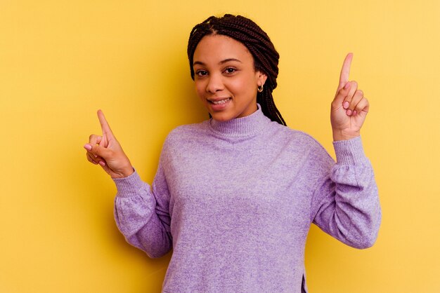 Jovem mulher afro-americana isolada em fundo amarelo apontando para diferentes espaços de cópia, escolhendo um deles, aparecendo com o dedo.