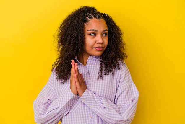 Jovem mulher afro-americana isolada em fundo amarelo orando, mostrando devoção, pessoa religiosa em busca de inspiração divina.