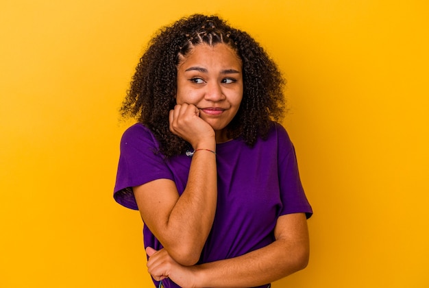 Jovem mulher afro-americana isolada em fundo amarelo, roendo as unhas, nervosa e muito ansiosa.