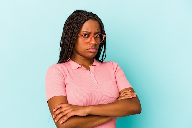 Jovem mulher afro-americana isolada em fundo azul suspeita, incerta, examinando você.