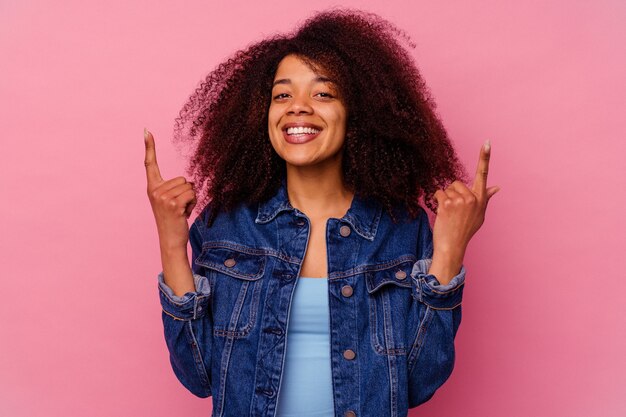 Jovem mulher afro-americana isolada em rosa indica com os dois dedos anteriores mostrando um espaço em branco.