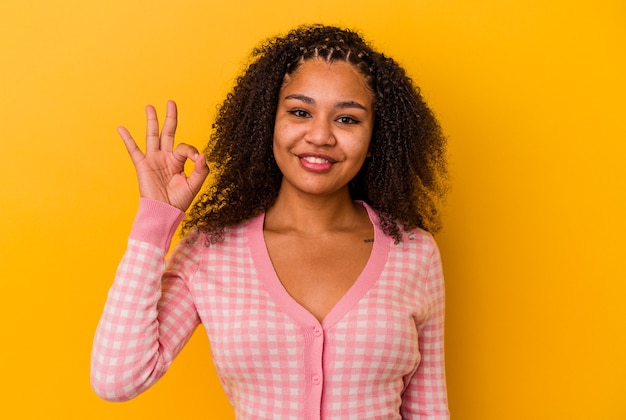 Jovem mulher afro-americana isolada em um fundo amarelo alegre e confiante, mostrando um gesto de ok.