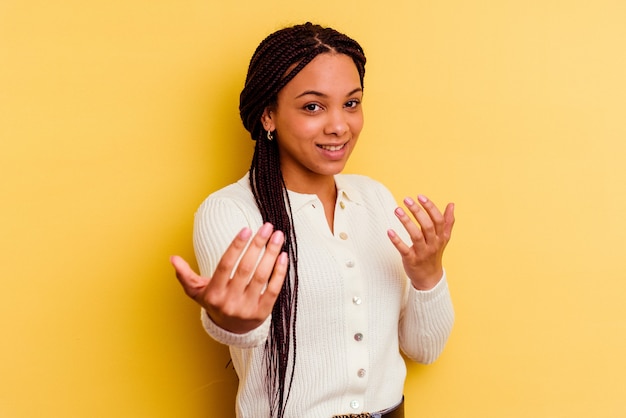 Jovem mulher afro-americana isolada em um fundo amarelo, apontando com o dedo para você como se fosse um convite para se aproximar.