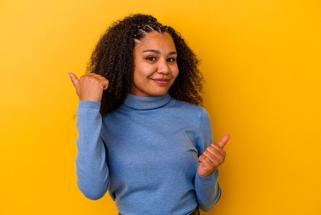 Jovem mulher afro-americana isolada em um fundo amarelo, levantando os dois polegares, sorrindo e confiante.