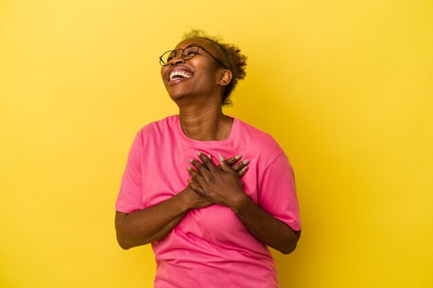 Jovem mulher afro-americana isolada em um fundo amarelo rindo mantendo as mãos no coração, o conceito de felicidade.