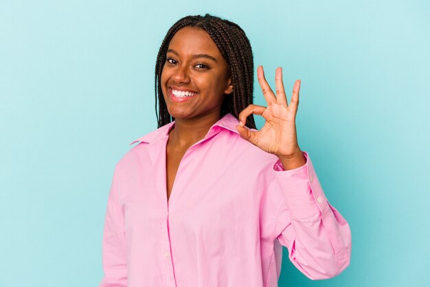 Jovem mulher afro-americana isolada em um fundo azul alegre e confiante, mostrando um gesto de ok.