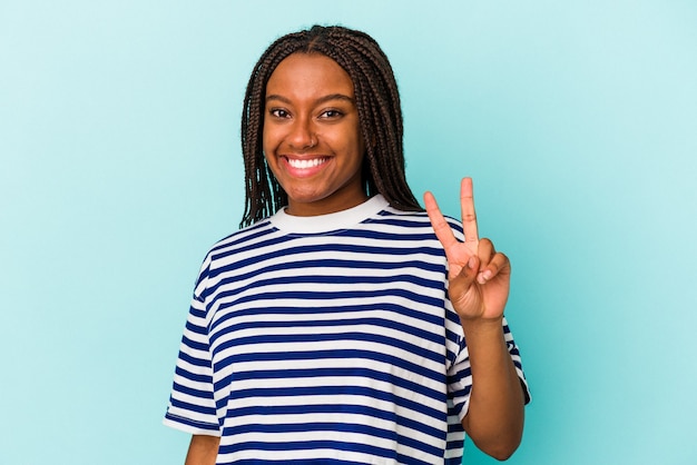 Jovem mulher afro-americana isolada em um fundo azul, mostrando sinal de vitória e sorrindo amplamente.