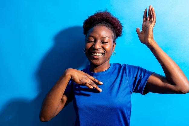 Jovem mulher afro-americana isolada em um fundo azul sorrindo e dançando sessão de estúdio