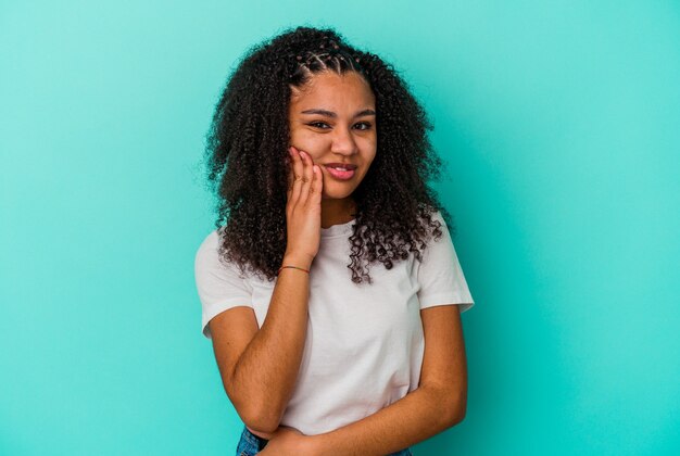 Jovem mulher afro-americana isolada em um fundo azul, tendo uma forte dor nos dentes, dor molar.